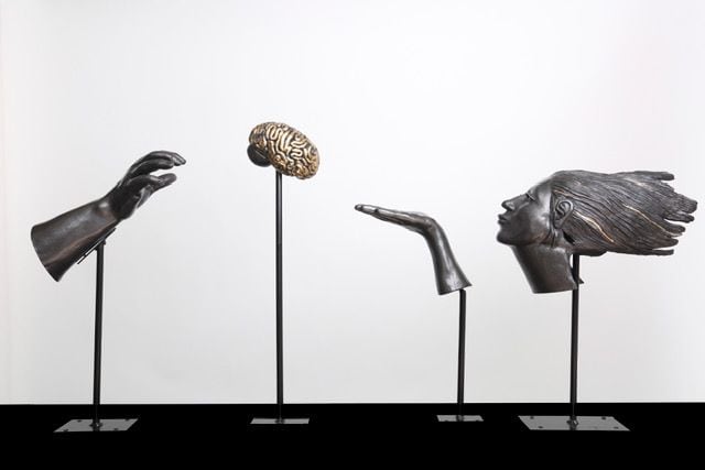 Fragments, a ceramic installation by Ireri Krueger of a hand, a brain, a blown kiss, and a windblown head on slender stands