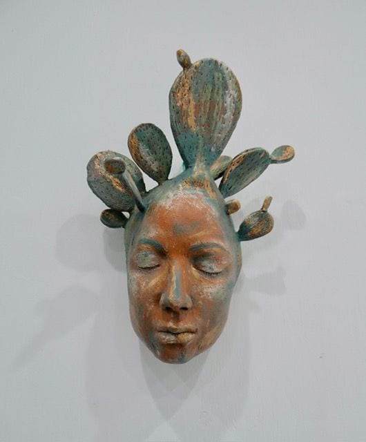 Nopal, a ceramic wall sculpture by Ireri Krueger of a serene face crowned with prickly pear cactus pads in teal and terracotta glaze
