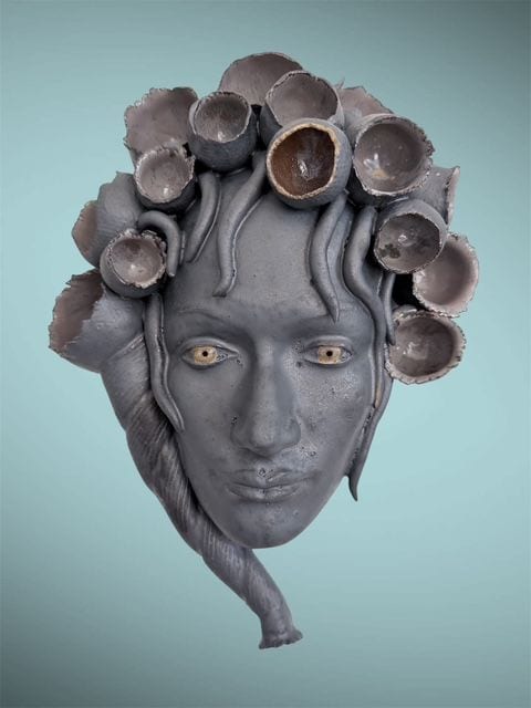 Vessels, a ceramic wall mask by Ireri Krueger of a grey face framed by hollow cup-like forms in place of hair
