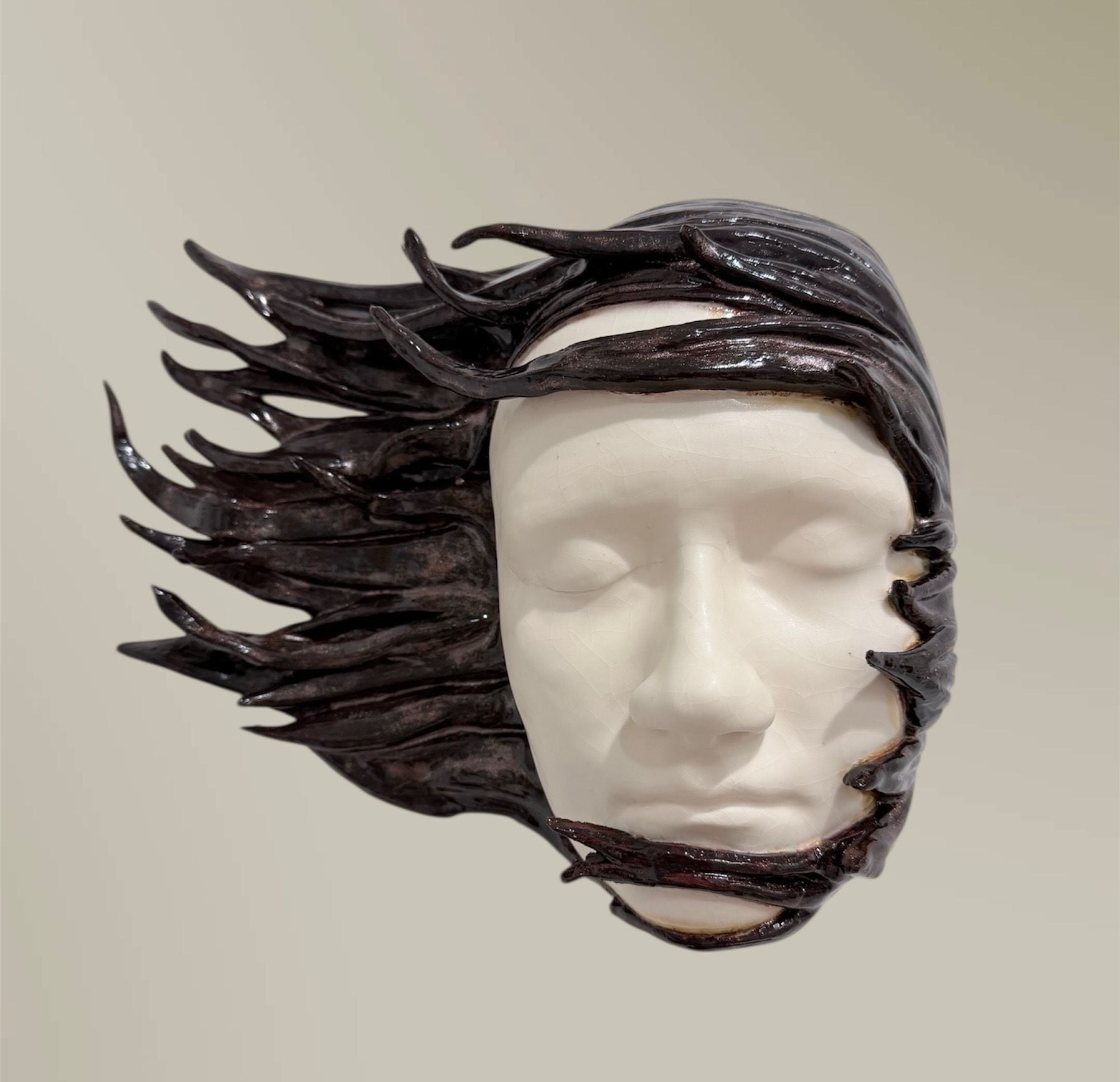 Windswept, a ceramic wall mask by Ireri Krueger of a calm white face framed by dark hair streaming in the wind